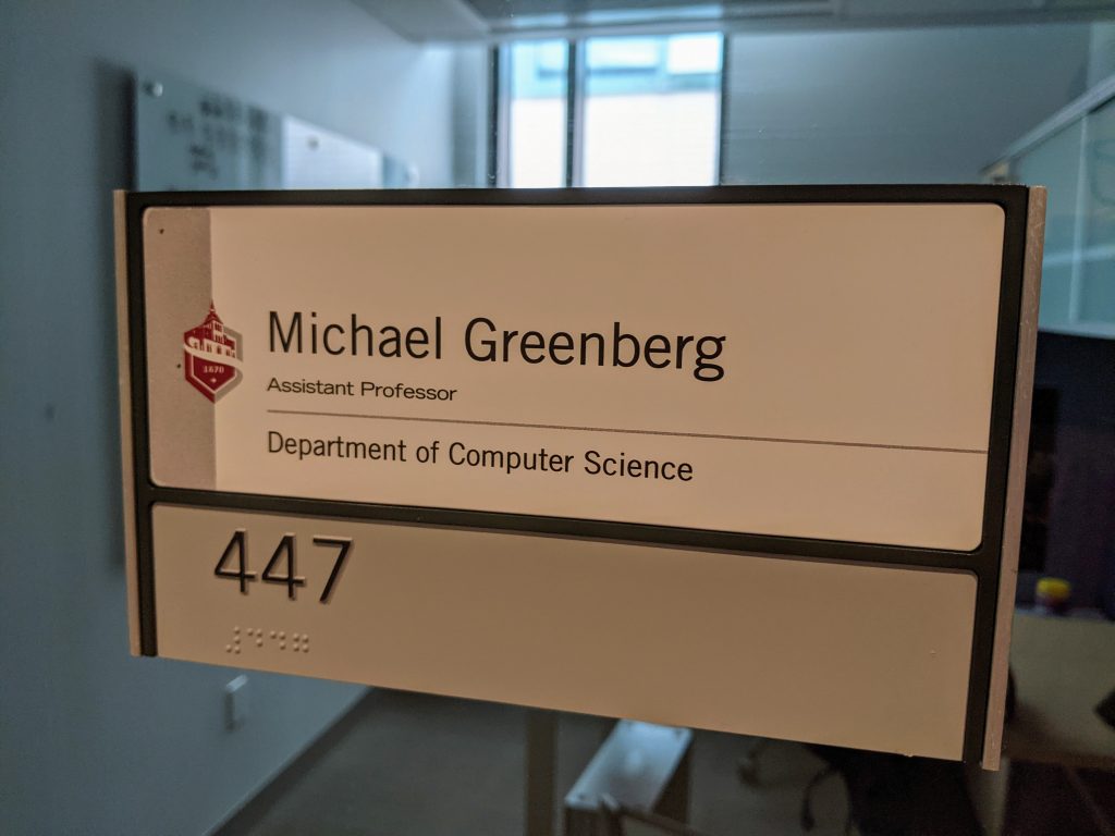 A photo of my office nameplate. The Stevens logo in red, with the following text:<p></p>Michael Greenberg Assistant Professor Department of Computer Science<p></p>447 447 (in Braille)