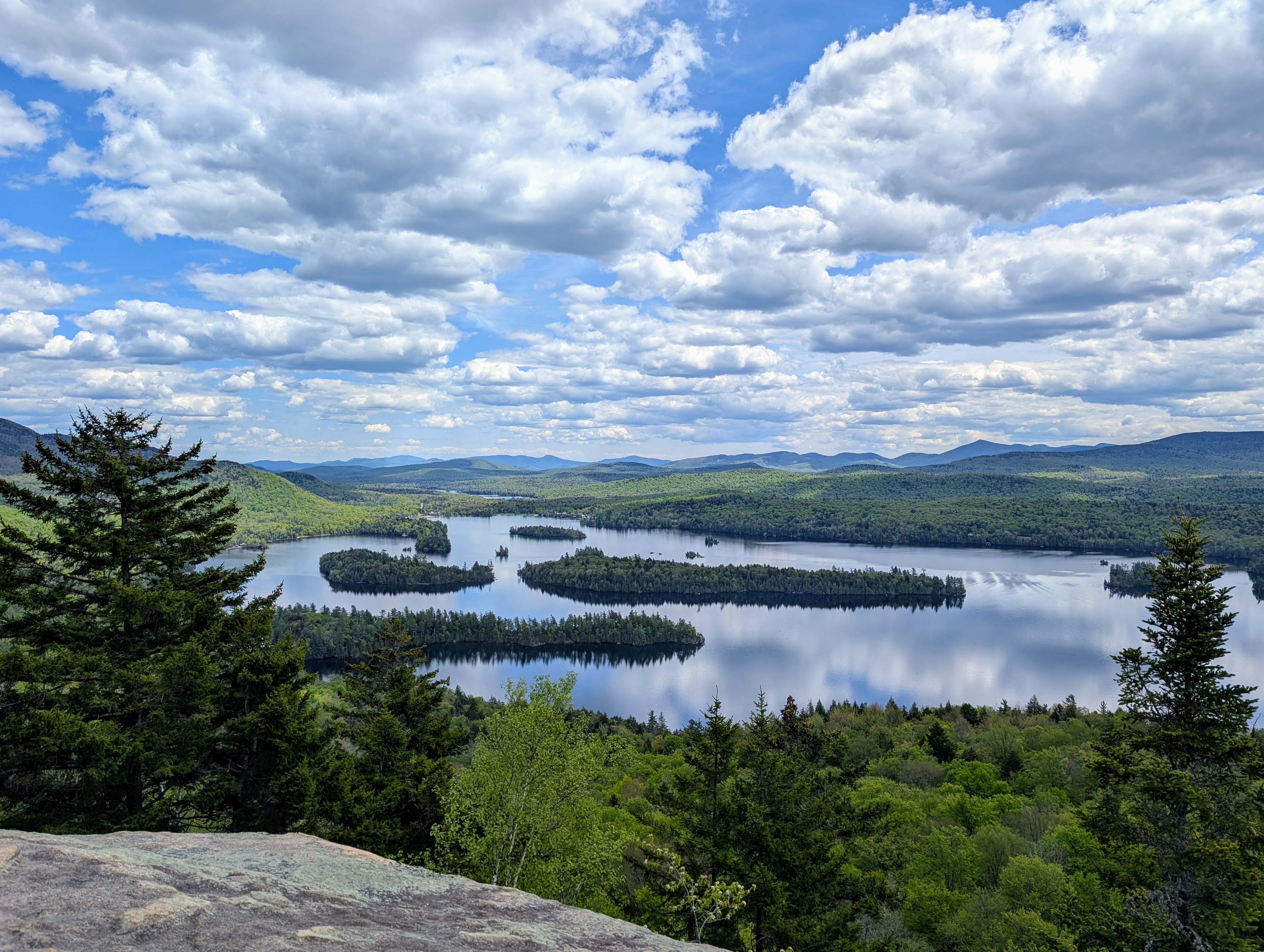 A beautiful lake is dotted with islands; mountains surround. It's very green; the sky is very blue; the clouds are fluffy.